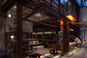 A warm and inviting restaurant interior with wooden floors and walls, featuring a dining table and chairs, and scattered bottles around the space