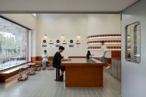 A casual coffee shop interior with a wooden counter, chairs, and dining tables, featuring cups and bottles, and a welcoming atmosphere