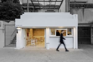 A cozy cafe with wooden chairs and tables, a doorway leading to the outside, and a person entering the space