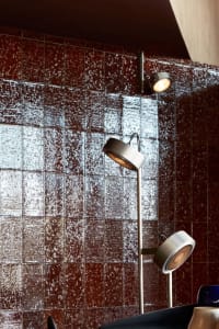 A modern room with a red brick wall featuring a tile pattern, lit by two ceiling lights, creating a warm atmosphere