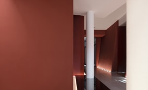 Narrow modern hallway with red walls, a white pillar, and natural light from a window