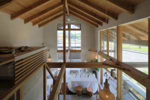 Open living space with wooden beams, two dining tables, chairs, potted plants, and decorative elements
