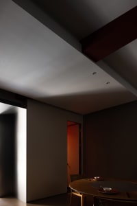 A dimly lit hallway with a gray wall and a doorway leading to another room
