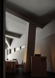 Dimly lit dining room with a wooden dining table and chairs, surrounded by white walls and warm lighting