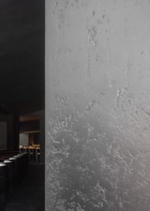 Empty dark room with a concrete wall and several chairs, giving a moody atmosphere