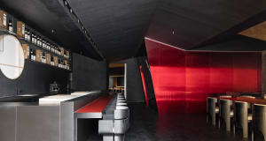 Modern restaurant interior with a long counter, red accents, and books scattered throughout, exuding a stylish and contemporary vibe