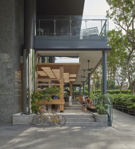 Modern interior space with a large glass wall, wooden frame, potted plants, and two chairs, featuring a contemporary design with natural elements