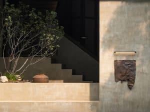 A modern staircase leads to a doorway in front of a concrete wall, flanked by two potted plants