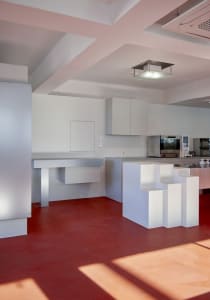 Open kitchen with white cabinets, red flooring, two sinks, and marble countertops in a modern and clean design