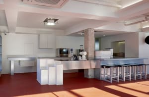 Industrial kitchen with a red floor, appliances, and seating, well-equipped for cooking and food storage