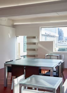 Modern dining space with a glass table surrounded by chairs, a city view through a window, and a contemporary atmosphere