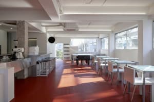 A modern restaurant interior with red tile flooring, clean lines, and natural light, featuring multiple tables and chairs in a welcoming atmosphere