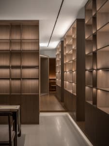 A calm and organized hallway with wooden walls and floors, lined with bookshelves and a chair, showcasing a collection of books