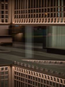 A modern hallway with a glass wall reflecting the surroundings, wooden panels on the walls, and well-lit space with natural or artificial light