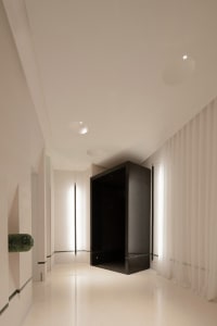 A clean and modern hallway with white walls and floors, lit by overhead lights, creating a calm and quiet atmosphere