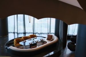 Sophisticated living space with a curved wall, seating areas, and a dining table, featuring a mix of materials and natural light