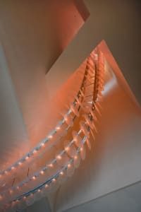 A modern stairwell with a glass chain link fence, illuminated by lights, creating a striking contrast between transparent and opaque elements