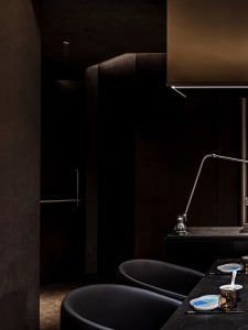 Dark modern kitchen with black cabinets, a sink area, oven, and refrigerator, and two chairs for seating