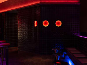 Bathroom with black walls, red accents, three round lights, a sink, and a bench, giving off a modern and sleek vibe