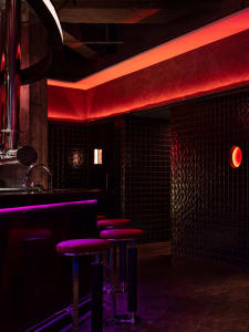 A modern bar area with a counter, stools, and sink, featuring black tile walls and inviting seating for patrons