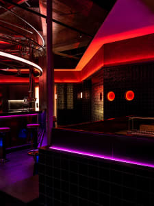 A lively bar with a purple neon glow, circular decorations, a counter with stools, and a sink, creating a welcoming atmosphere