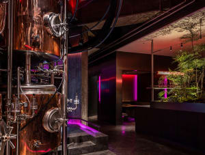 An industrial space with a large copper vat, pipes, wires, and potted plants, conveying a sense of functionality and industrial design