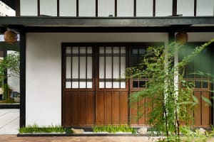 A simple Asian-style house with wooden doors and windows, surrounded by greenery and a clean white exterior