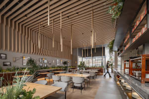 Modern restaurant interior with wooden floors, ceiling beams, and potted plants, featuring comfortable seating and a cozy atmosphere