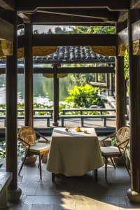 An Asian-style patio area with a dining table and chairs under a wooden pavilion, surrounded by a relaxed and inviting atmosphere