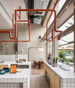 A modern kitchen with red pipes, wooden floors, and white walls, featuring a dining table and various decorative items