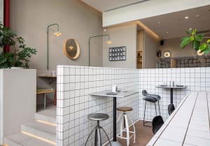 A cozy dining area with two tables and chairs, surrounded by tiled walls and kitchen, with various items and equipment visible