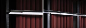 A room with red fabric curtains in front of windows, one with a person standing near the window, the other empty