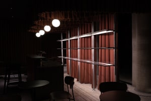 A modern restaurant interior with a counter and three chairs, a cozy atmosphere, and a curtain covering part of the window
