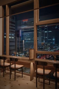 Elegant restaurant interior with modern design elements, chairs, and a stunning city skyline view through a large window at night