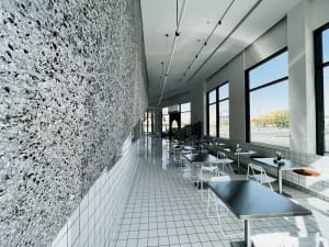 Empty modern restaurant with white tile floor, large window, and dining tables and chairs