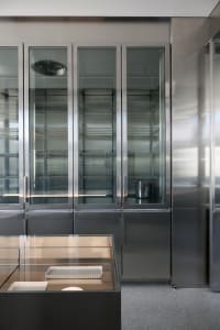 Modern kitchen with stainless steel appliances, two refrigerators, three ovens, and a sink, surrounded by cabinets and drawers