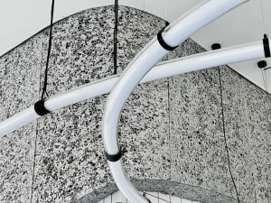 A modern art gallery with a large white marble sculpture hanging from the ceiling, set against a minimalist background