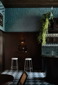 A modern bar with a black countertop, blue walls, and three stools, creating a relaxed and inviting atmosphere