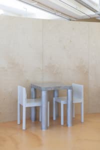 Empty dining area with two white chairs and a small metal table in a minimalist space with clean lines and no additional decorations