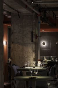 Dimly lit restaurant interior with a dining table, chairs, and wine glasses, surrounded by stone walls