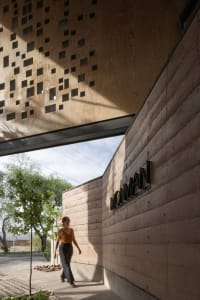 A woman walks through a calm and serene indoor space with a stone wall and a natural backdrop of trees