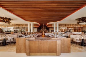 Warm and inviting restaurant interior with wooden floors and walls, featuring dining tables and chairs, and wine glasses on some tables
