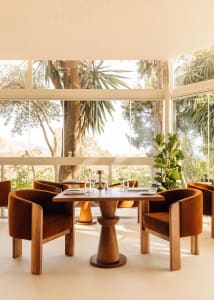 A modern restaurant interior with tables, chairs, and potted plants, set with wine glasses and cutlery, creating a sophisticated atmosphere
