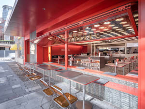 A modern Asian restaurant interior with a red accent wall, natural light, and dining tables and chairs