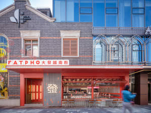 Lively Asian restaurant with red walls, orange trim, and multiple tables and chairs in a dining area with people seated and standing