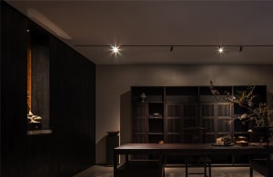 Cozy living space with wooden floors and walls, a dining table, chairs, and decorative vases, bathed in warm lighting