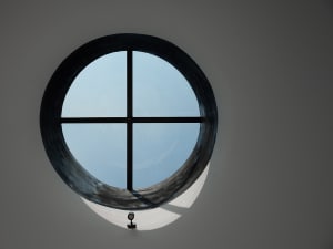 A dimly lit scene with a round window featuring a black frame and a small lamp inside