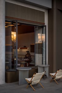 A well-lit dining area with a woman sitting at a table near a window, surrounded by multiple chairs and a comfortable atmosphere