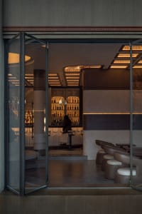 A lively bar scene with wooden accents, multiple chairs, and a large number of bottles on display, set against a warm and inviting atmosphere