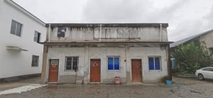 Aged building with a weathered concrete facade, featuring two doors and two windows, with a neglected appearance
